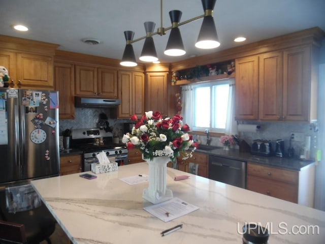 kitchen with stainless steel appliances, brown cabinetry, a sink, and under cabinet range hood