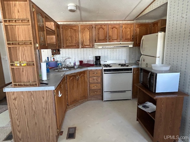 kitchen with white appliances, visible vents, brown cabinets, a sink, and exhaust hood