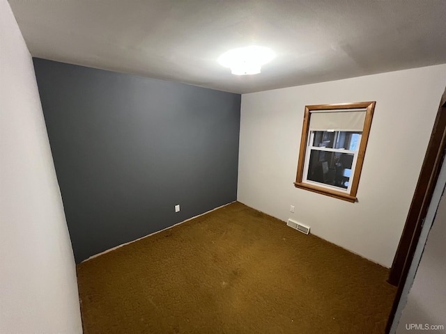 spare room featuring dark colored carpet and visible vents