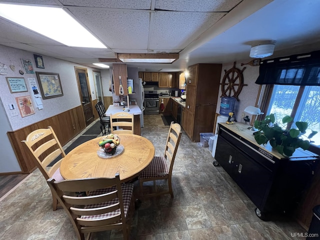 dining room featuring wood walls, stone finish flooring, a drop ceiling, and wainscoting