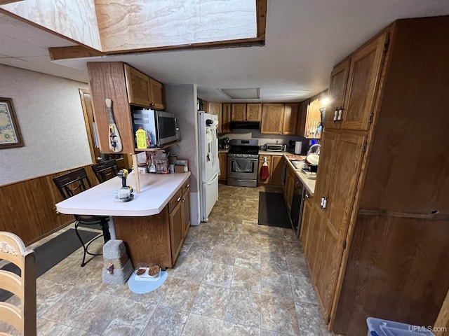 kitchen featuring light countertops, appliances with stainless steel finishes, brown cabinetry, and wainscoting