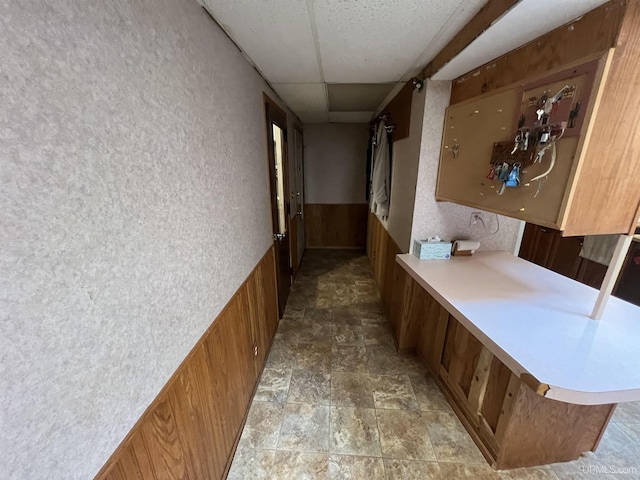 hall featuring a wainscoted wall, a drop ceiling, stone finish floor, and wood walls