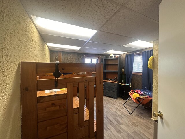 bedroom with a drop ceiling, a textured wall, wood walls, and wood finished floors