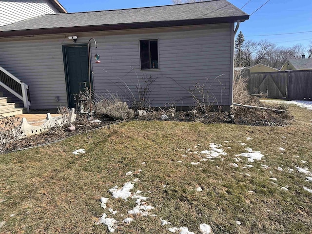 exterior space featuring roof with shingles, a lawn, and fence