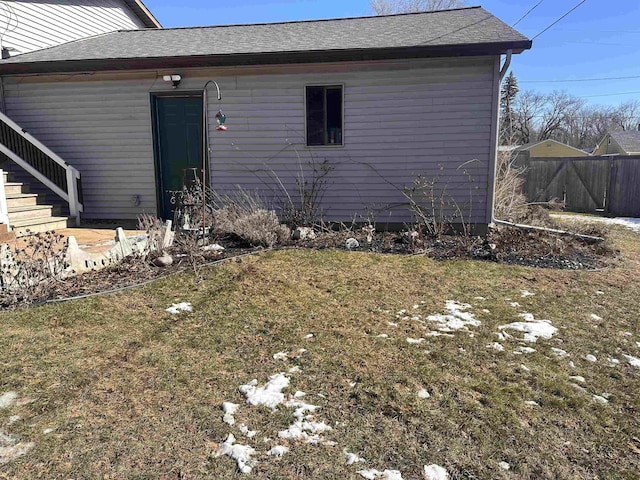 view of side of home featuring stairway, a shingled roof, fence, and a yard