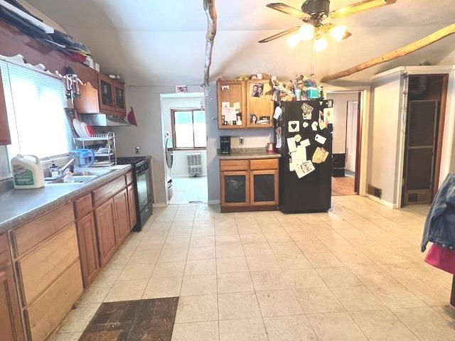 kitchen featuring light tile patterned floors, glass insert cabinets, brown cabinets, black appliances, and a sink