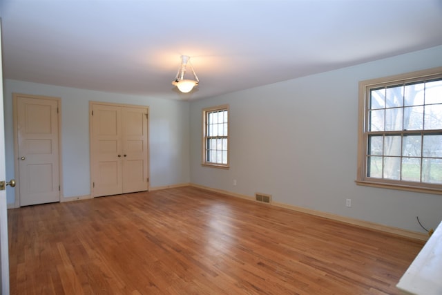 unfurnished bedroom featuring light wood-type flooring, a closet, visible vents, and baseboards