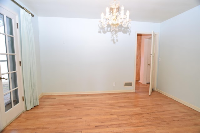 spare room featuring light wood-style floors, visible vents, baseboards, and a chandelier