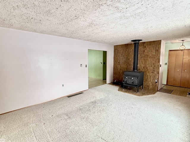 unfurnished living room featuring a textured ceiling, carpet flooring, and a wood stove