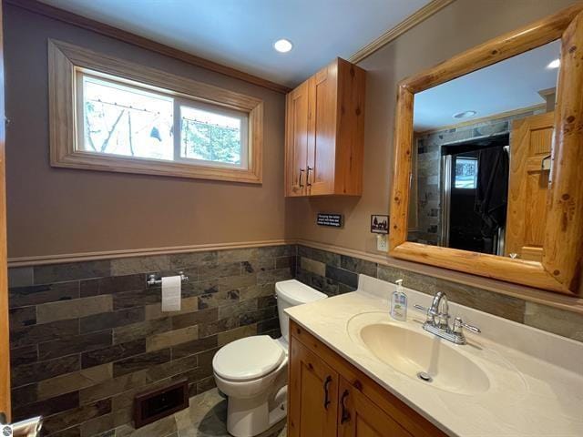 bathroom featuring wainscoting, vanity, toilet, and tile walls