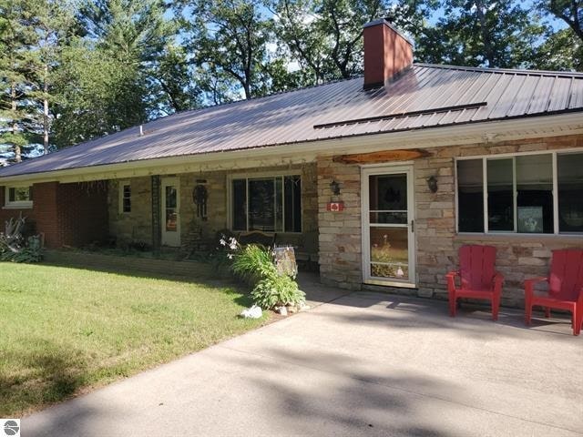 rear view of property featuring stone siding, a chimney, metal roof, and a yard