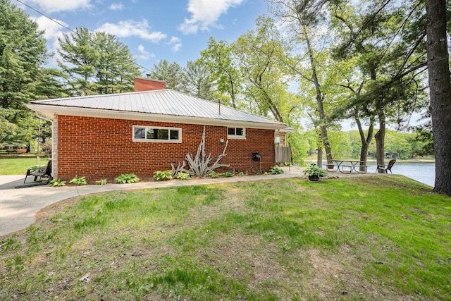 7836 W Perch Lake Dr, Lake, MI 48632 - view of home's exterior featuring a chimney, a yard, brick siding, and metal roof