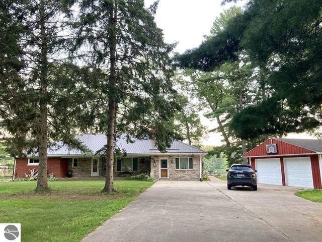 single story home with an outbuilding, metal roof, a detached garage, stone siding, and a front lawn