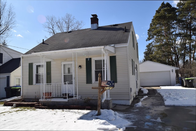 bungalow featuring an outbuilding, roof with shingles, a detached garage, a chimney, and covered porch