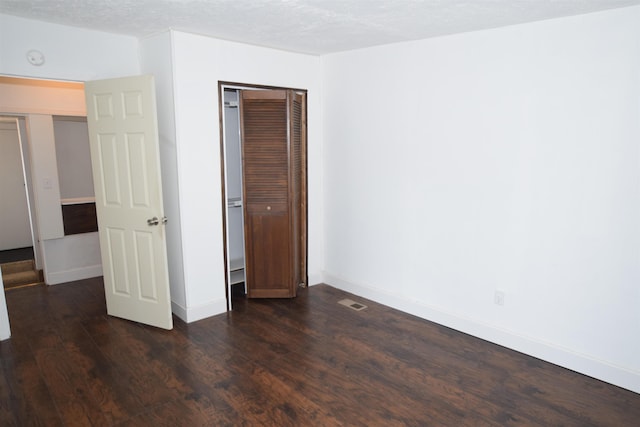 unfurnished bedroom featuring a textured ceiling, a closet, dark wood finished floors, and baseboards