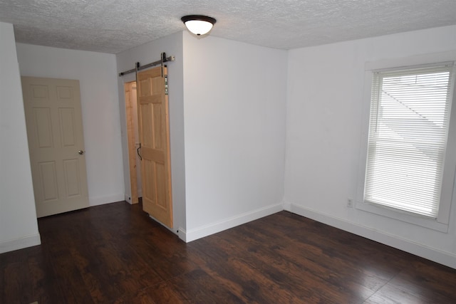 unfurnished room featuring dark wood-type flooring, plenty of natural light, baseboards, and a barn door