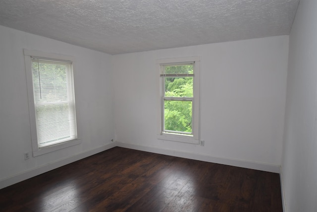 empty room featuring a textured ceiling, baseboards, and dark wood-style flooring