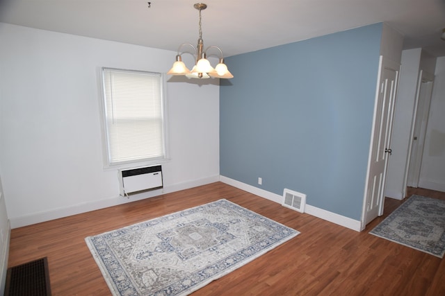 empty room with visible vents, a notable chandelier, baseboards, and wood finished floors