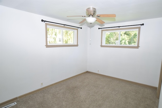 carpeted empty room featuring a ceiling fan, plenty of natural light, visible vents, and baseboards