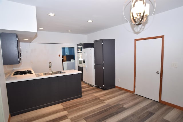 kitchen featuring washing machine and clothes dryer, light wood-style flooring, a sink, white appliances, and a peninsula