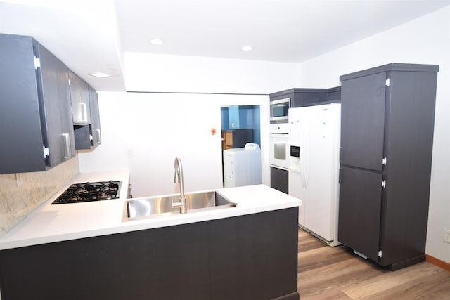 kitchen with white appliances, washer and clothes dryer, a peninsula, light wood-style floors, and a sink