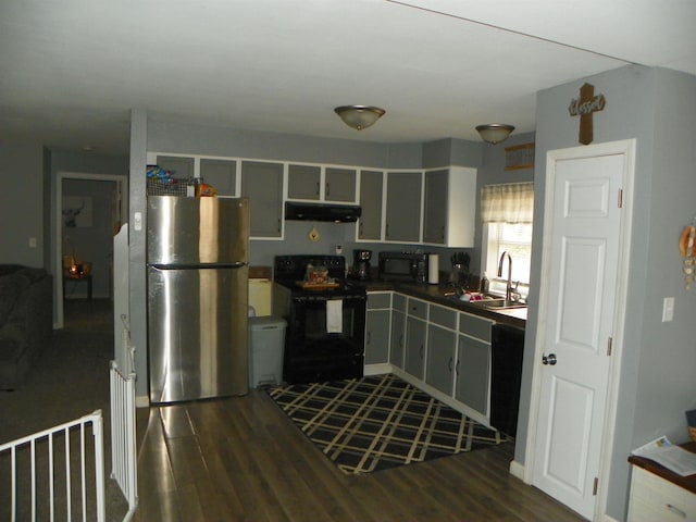 kitchen with dark wood-style flooring, dark countertops, a sink, under cabinet range hood, and black appliances