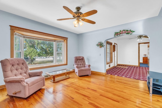 living area featuring arched walkways, wood finished floors, a ceiling fan, and baseboards