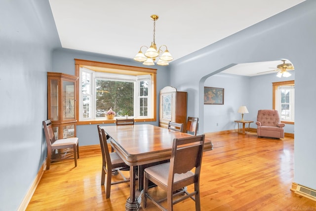 dining area featuring arched walkways, a notable chandelier, visible vents, light wood-type flooring, and baseboards