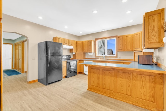 kitchen with arched walkways, a peninsula, under cabinet range hood, black appliances, and a sink