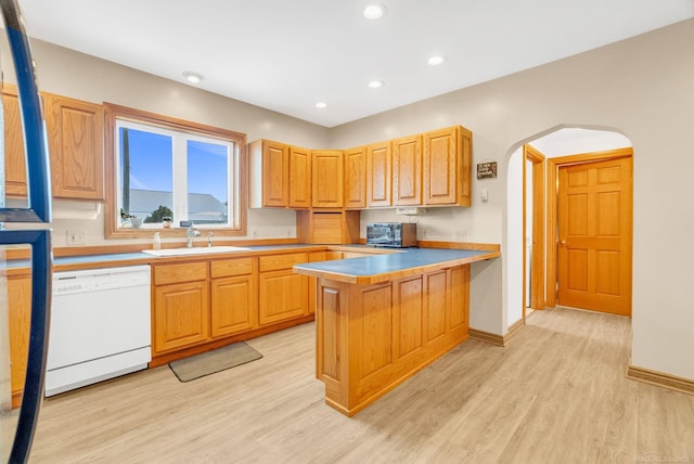 kitchen featuring arched walkways, white dishwasher, a sink, light wood-type flooring, and a peninsula