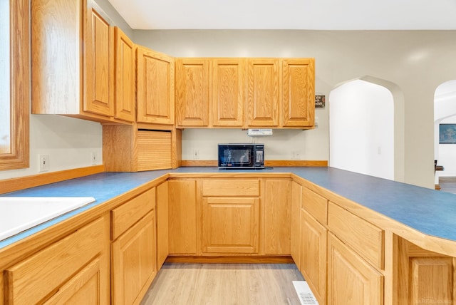 kitchen with arched walkways, black microwave, and light wood-style floors