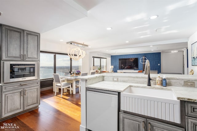 kitchen with light stone counters, recessed lighting, a sink, dishwasher, and dark wood finished floors