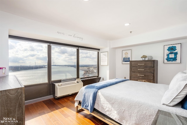 bedroom featuring an AC wall unit, a water view, hardwood / wood-style flooring, and recessed lighting