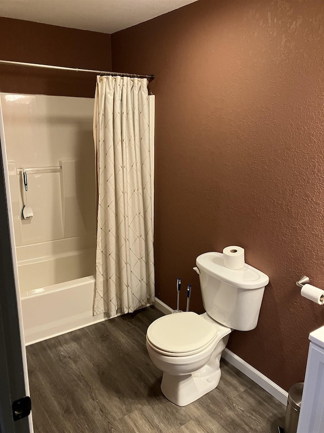 bathroom with toilet, baseboards, wood finished floors, and shower / tub combo with curtain