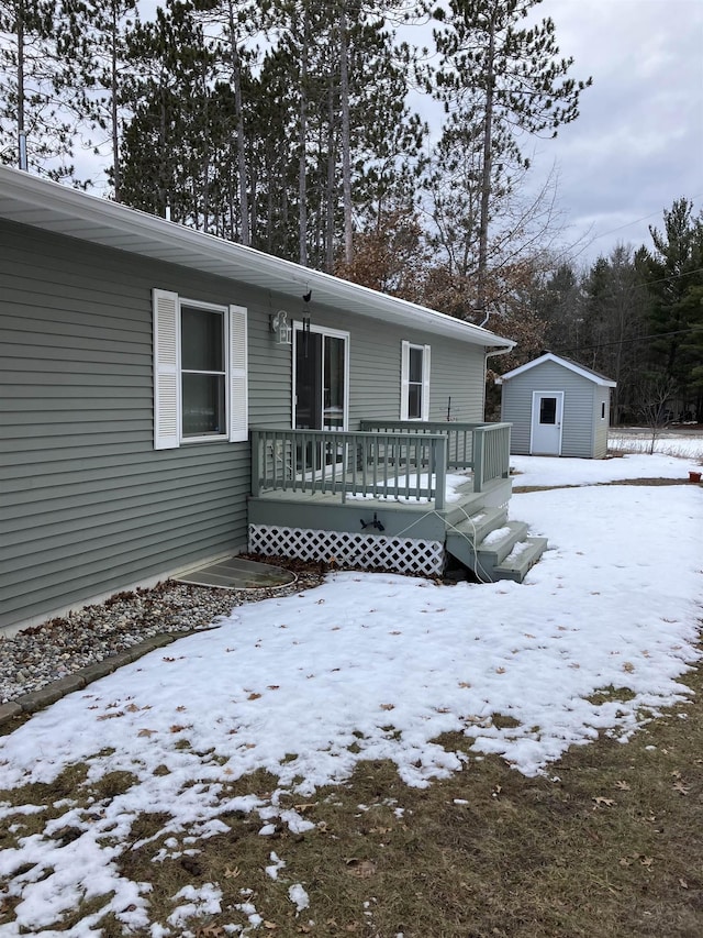 snow covered house featuring a storage shed, a deck, and an outdoor structure