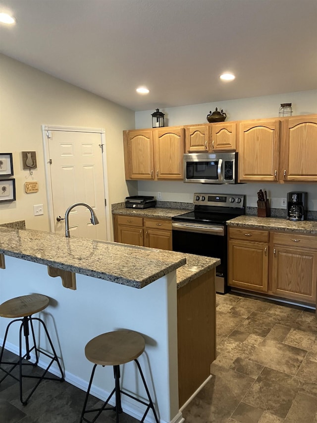 kitchen with recessed lighting, a peninsula, a breakfast bar, a sink, and appliances with stainless steel finishes