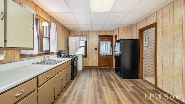 kitchen featuring a drop ceiling, a sink, light countertops, black appliances, and light wood finished floors