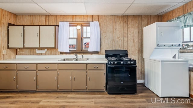 kitchen with stacked washer and dryer, a sink, wood walls, and black range with gas stovetop