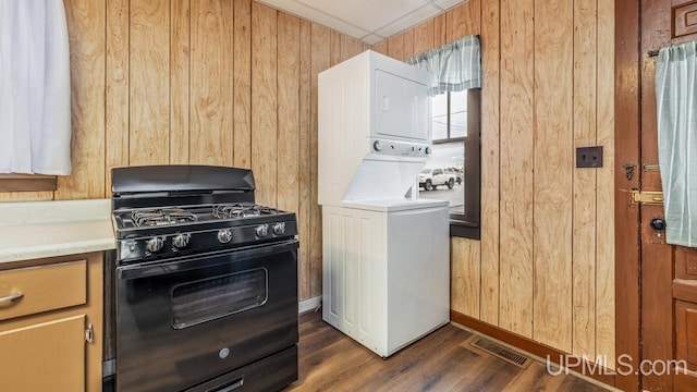 laundry area featuring laundry area, wooden walls, visible vents, stacked washer and clothes dryer, and dark wood-style floors