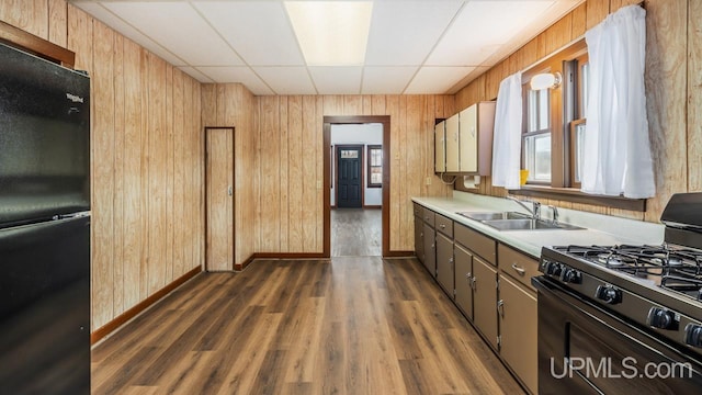 kitchen featuring wooden walls, dark wood-style flooring, light countertops, black appliances, and a sink