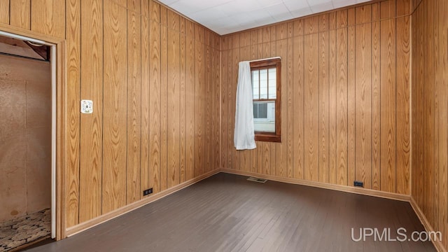 unfurnished room with wood walls, wood finished floors, visible vents, and baseboards