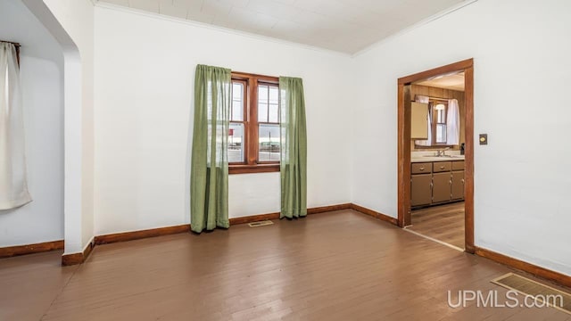 unfurnished room with arched walkways, visible vents, ornamental molding, wood finished floors, and baseboards