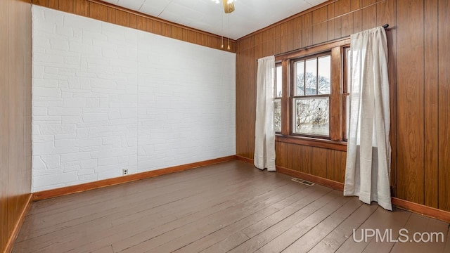 empty room featuring baseboards, hardwood / wood-style flooring, visible vents, and wooden walls