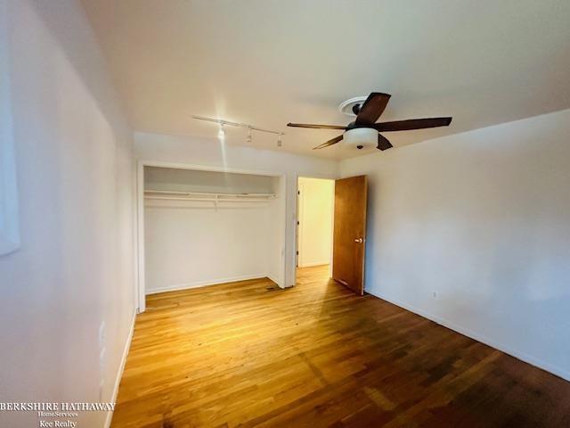 unfurnished bedroom featuring a closet, ceiling fan, track lighting, and wood finished floors