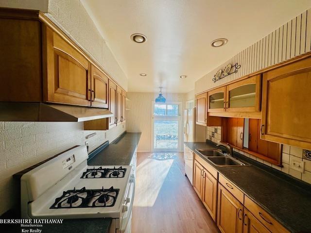 kitchen with white gas stove, a sink, light wood-type flooring, dark countertops, and glass insert cabinets