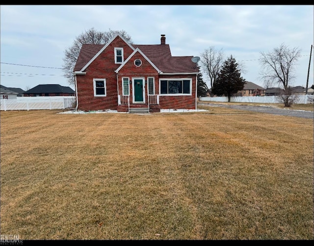 view of front facade with a chimney, a front yard, fence, and brick siding