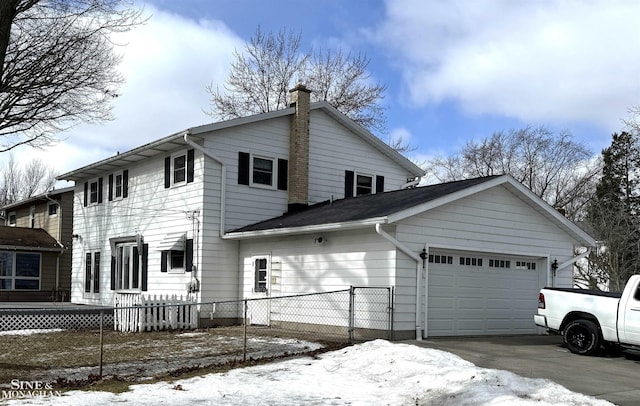 snow covered property with driveway, fence, a chimney, and an attached garage