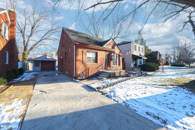 view of front of property featuring driveway, brick siding, a detached garage, and an outbuilding