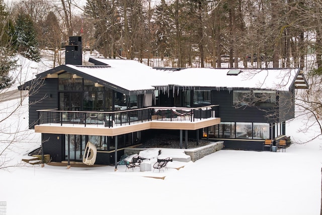 snow covered rear of property with a chimney and a wooden deck