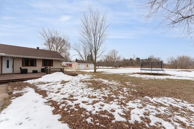 snowy yard featuring a trampoline, an outbuilding, and a deck